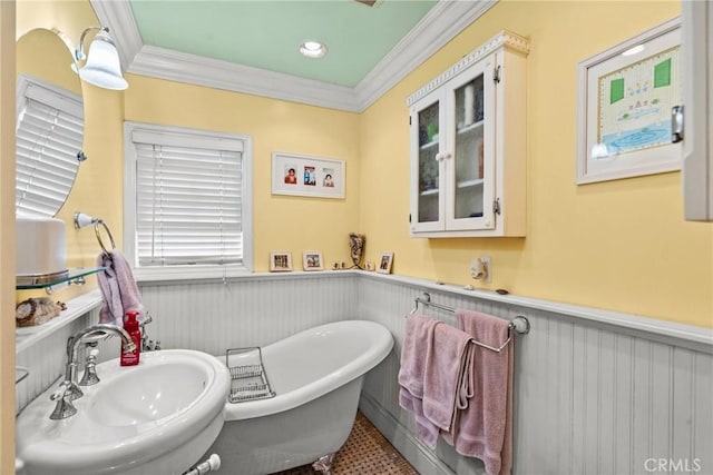 full bathroom with crown molding, a soaking tub, wainscoting, and a sink