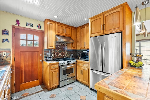 kitchen with pendant lighting, tile countertops, stainless steel appliances, tasteful backsplash, and under cabinet range hood