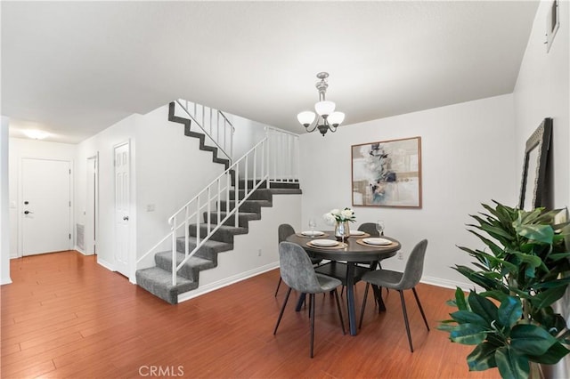 dining area with a chandelier, baseboards, wood finished floors, and stairway