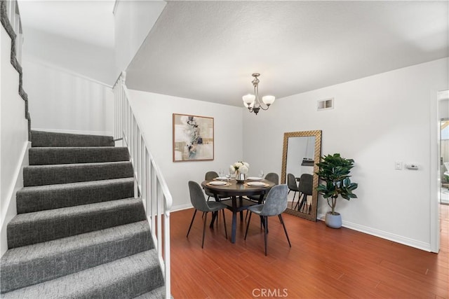 dining area with an inviting chandelier, visible vents, wood finished floors, and stairway