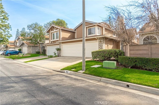 view of front of house with an attached garage, a front yard, fence, stone siding, and driveway