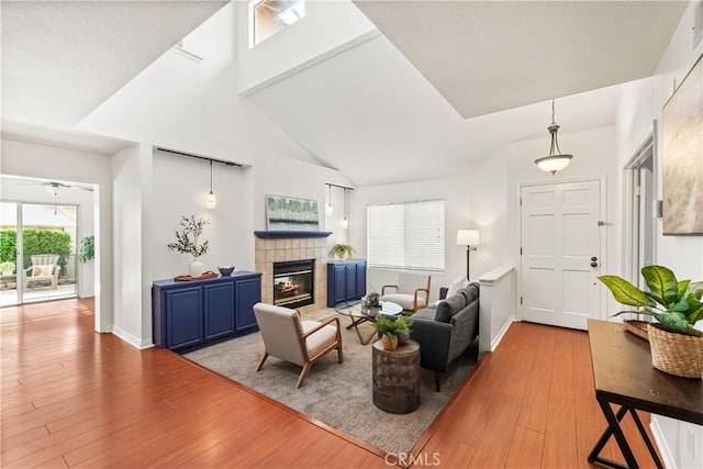 living area featuring a fireplace, high vaulted ceiling, light wood-type flooring, and baseboards