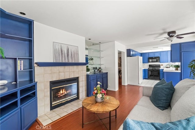 living room with ceiling fan, a tile fireplace, and wood finished floors