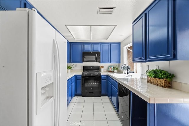 kitchen featuring black appliances, visible vents, blue cabinetry, light tile patterned floors, and a sink