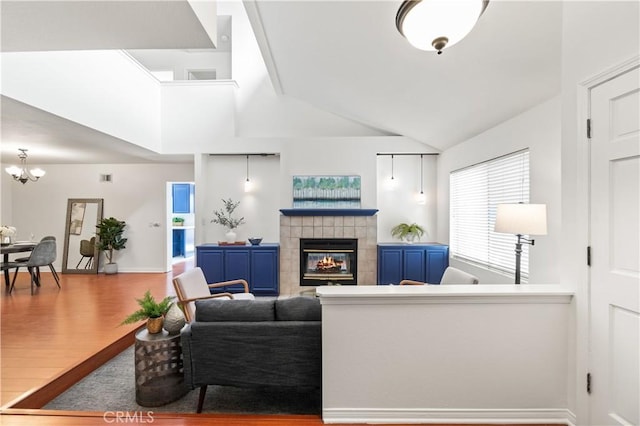 living area with a notable chandelier, visible vents, a tile fireplace, lofted ceiling, and wood finished floors