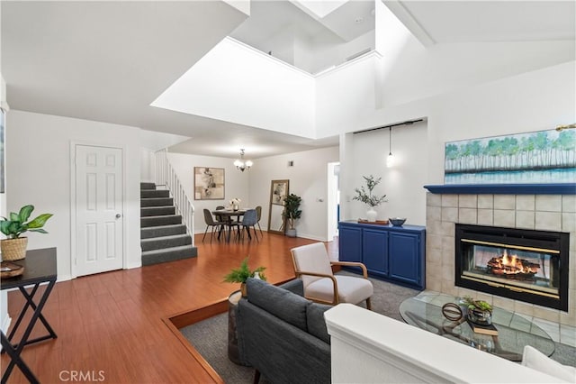 living area featuring a chandelier, a tiled fireplace, baseboards, stairs, and wood finished floors