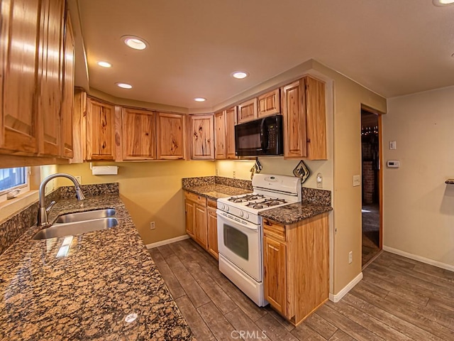 kitchen with sink, dark wood-type flooring, dark stone countertops, and white range with gas cooktop