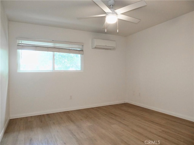 spare room featuring a ceiling fan, a wall unit AC, baseboards, and wood finished floors