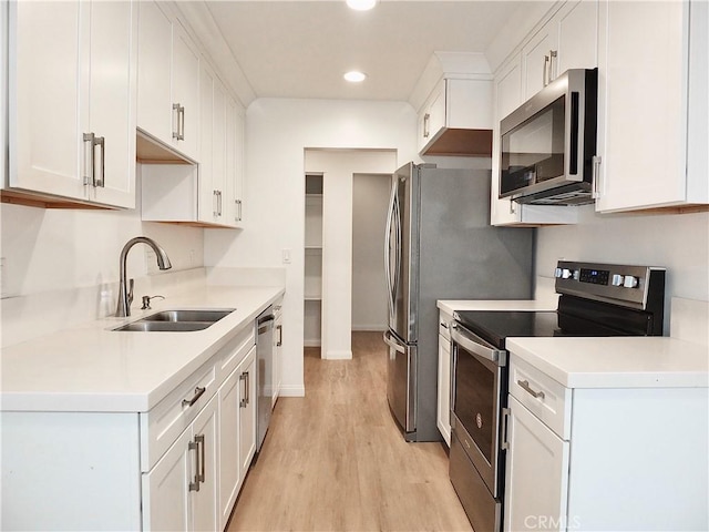 kitchen with stainless steel appliances, light countertops, light wood-style floors, white cabinetry, and a sink