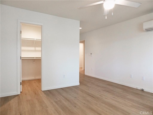 unfurnished bedroom with baseboards, wood finished floors, a walk in closet, an AC wall unit, and a closet