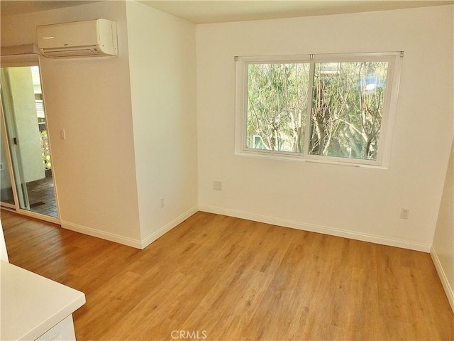 empty room with an AC wall unit, light wood-type flooring, and baseboards