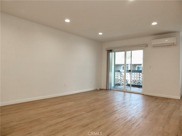 unfurnished room with light wood-type flooring, a wall mounted air conditioner, baseboards, and recessed lighting