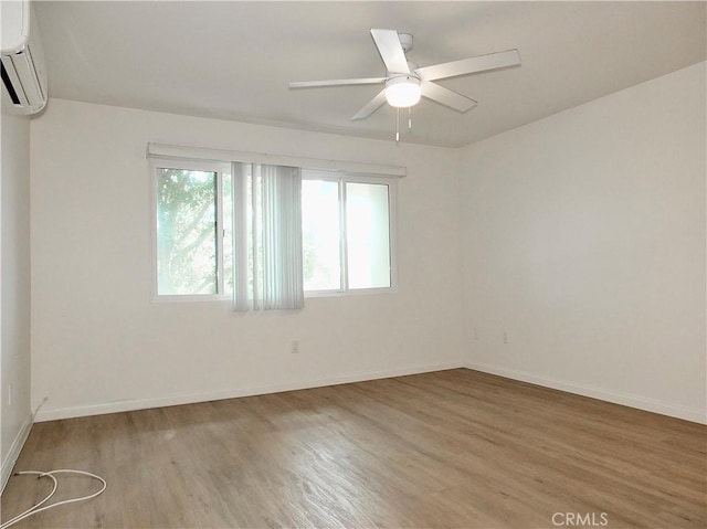 spare room with a wall unit AC, wood finished floors, a ceiling fan, and baseboards