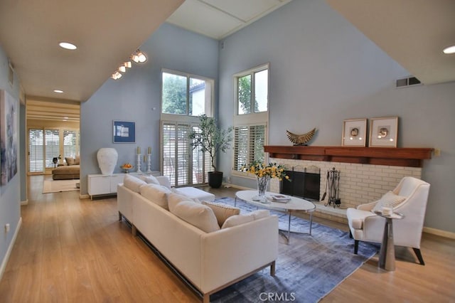 living area with a healthy amount of sunlight, a brick fireplace, visible vents, light wood-style floors, and a towering ceiling