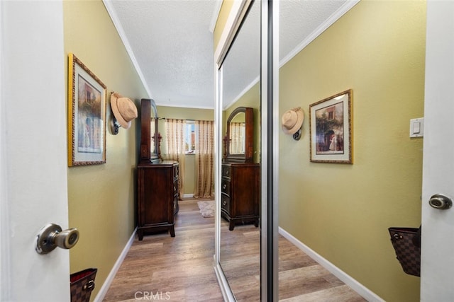 hall with a textured ceiling, ornamental molding, wood finished floors, and baseboards