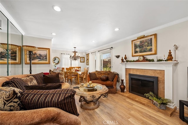 living room with a notable chandelier, recessed lighting, wood finished floors, ornamental molding, and a glass covered fireplace