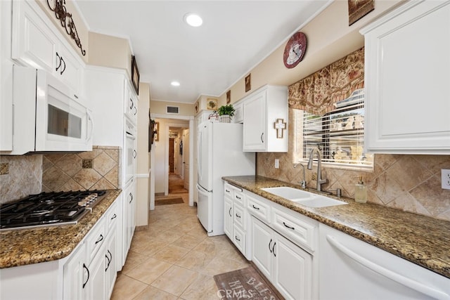 kitchen with white appliances, a sink, visible vents, white cabinets, and dark stone counters