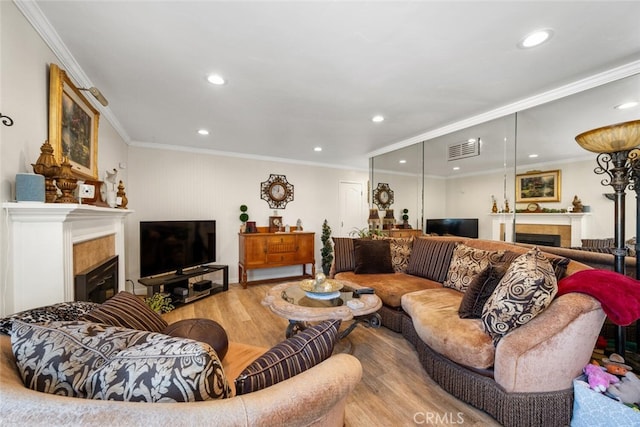 living area with ornamental molding, visible vents, a tiled fireplace, and wood finished floors