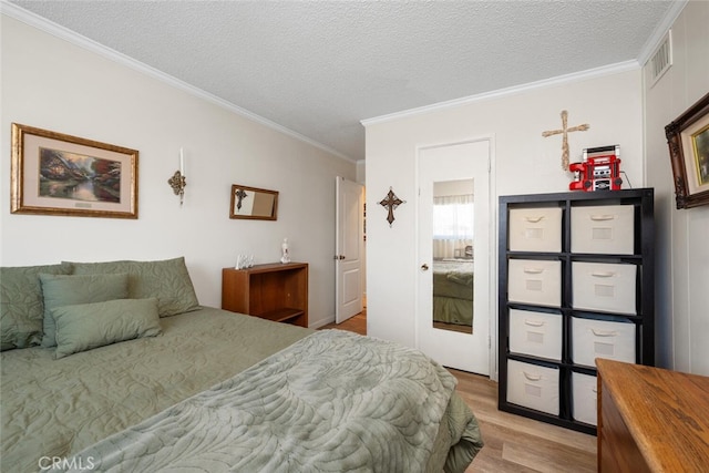 bedroom featuring light wood finished floors, visible vents, a textured ceiling, and ornamental molding