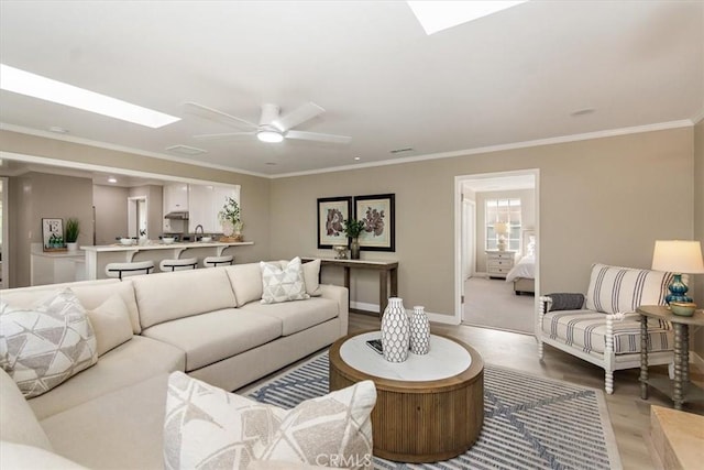 living room with ceiling fan, a skylight, light wood-style flooring, and crown molding