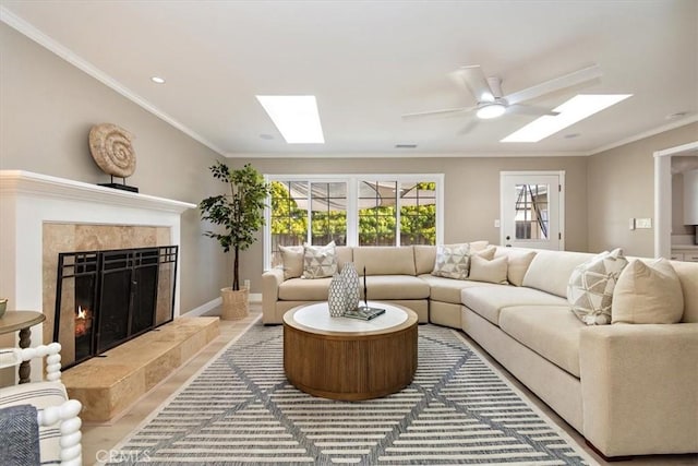 living room featuring a skylight, ornamental molding, a high end fireplace, a ceiling fan, and baseboards