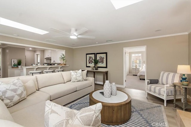 living room with a skylight, ceiling fan, ornamental molding, and light wood-style floors