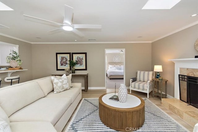 living room featuring wood finished floors, a ceiling fan, baseboards, a high end fireplace, and crown molding