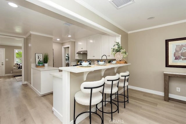 kitchen with a peninsula, a kitchen bar, visible vents, and under cabinet range hood