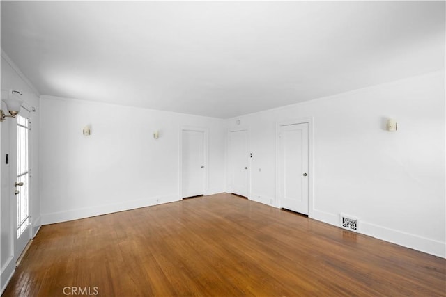 empty room with a wealth of natural light, visible vents, baseboards, and wood finished floors