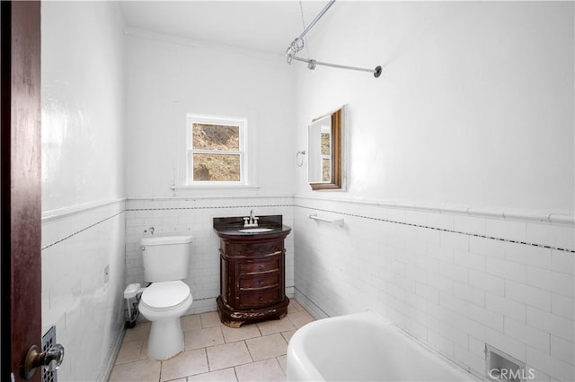 full bath with a tub to relax in, wainscoting, toilet, tile patterned floors, and vanity
