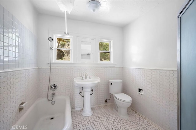 bathroom featuring tile patterned flooring, toilet, a washtub, a wainscoted wall, and tile walls