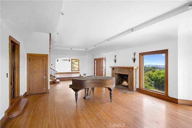 rec room featuring a brick fireplace, baseboards, and light wood finished floors
