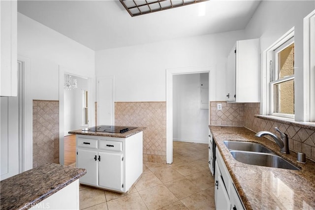 kitchen with black electric stovetop, white cabinetry, dark stone counters, and a sink