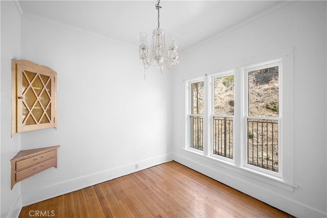 unfurnished dining area featuring a chandelier, baseboards, wood finished floors, and crown molding