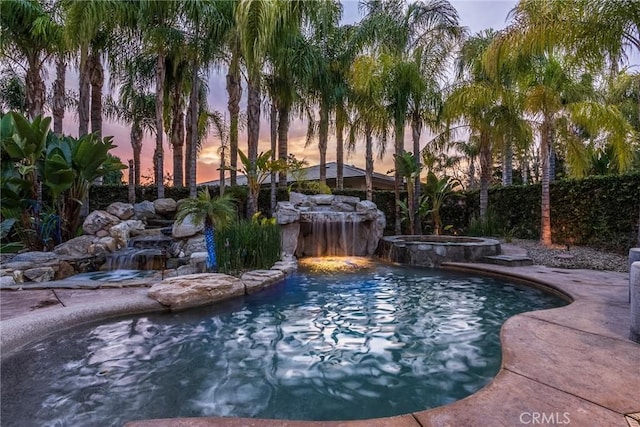 pool at dusk featuring an in ground hot tub