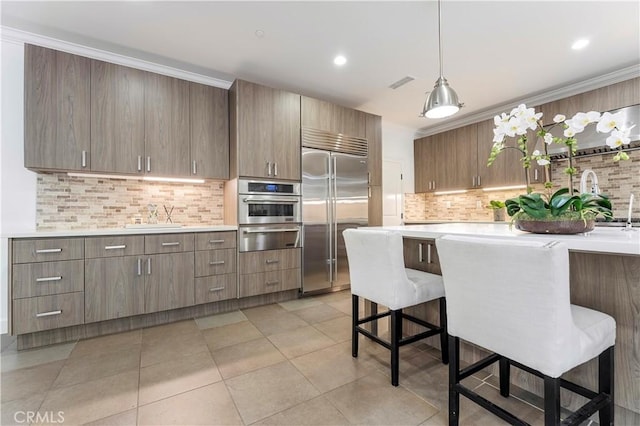 kitchen featuring a breakfast bar area, stainless steel appliances, crown molding, light countertops, and a warming drawer