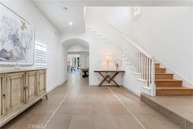 interior space featuring light tile patterned floors, baseboards, arched walkways, stairs, and recessed lighting