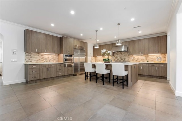 kitchen featuring crown molding, appliances with stainless steel finishes, a kitchen bar, and under cabinet range hood