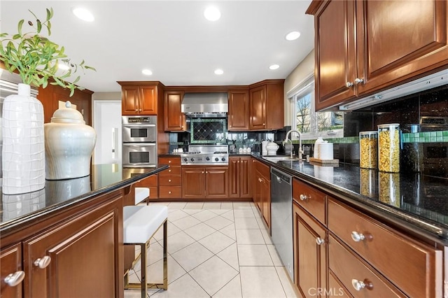 kitchen featuring sink, dark stone counters, appliances with stainless steel finishes, wall chimney range hood, and light tile patterned flooring