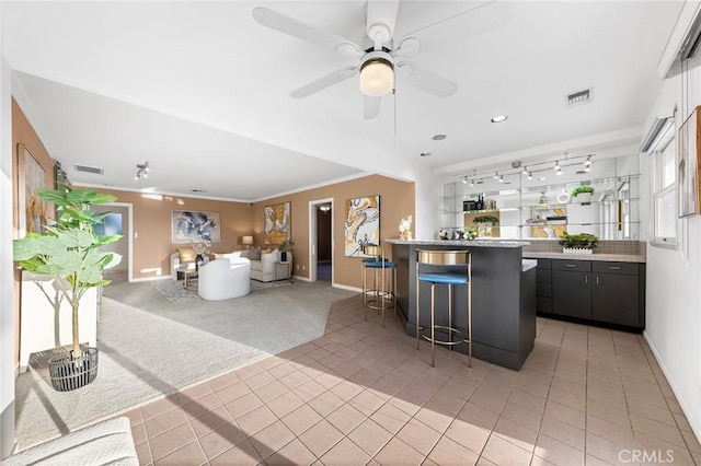 interior space featuring a kitchen breakfast bar, a kitchen island, carpet, crown molding, and ceiling fan