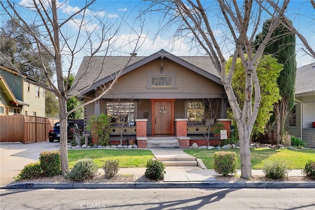 bungalow-style house with roof with shingles, fence, a porch, and a front yard