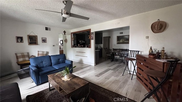 living area with a textured ceiling, ceiling fan, visible vents, and light wood finished floors