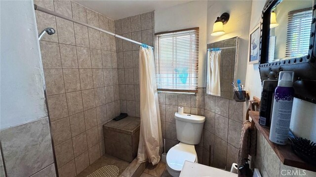 full bath with toilet, tiled shower, and tile walls