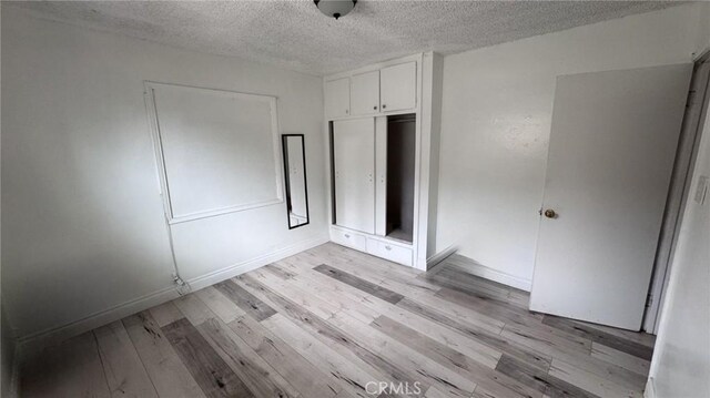unfurnished bedroom with baseboards, a closet, light wood-style flooring, and a textured ceiling