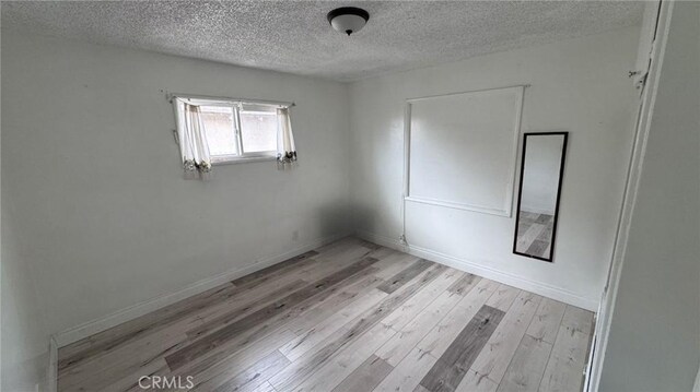 unfurnished room featuring baseboards, a textured ceiling, and light wood-style flooring