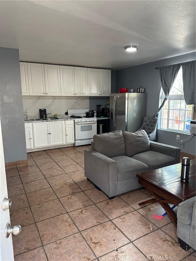 kitchen featuring light stone counters, a textured ceiling, white range with gas cooktop, white cabinetry, and stainless steel fridge with ice dispenser