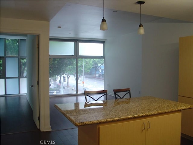 kitchen with a kitchen island, light stone countertops, a wealth of natural light, and pendant lighting