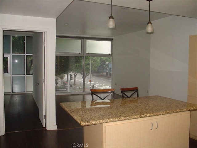 kitchen featuring dark wood-type flooring, decorative light fixtures, a kitchen island, and light stone counters