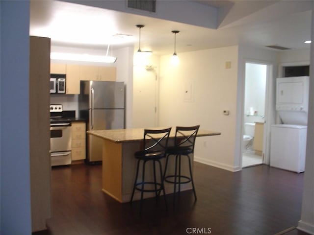 kitchen featuring stacked washer and clothes dryer, dark wood-style floors, stainless steel appliances, visible vents, and a breakfast bar area