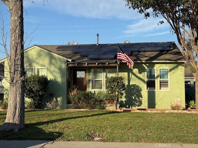 view of front of house featuring solar panels, a front lawn, and stucco siding